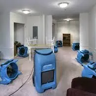 Room with several blue portable fans on the floor and a table turned upside down in the center.