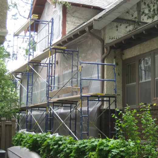 Scaffolding around a brick townhouse exterior with covered walkways and shrubs in front