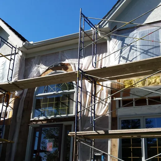 Scaffolding around a house under construction with white siding and a gray roof