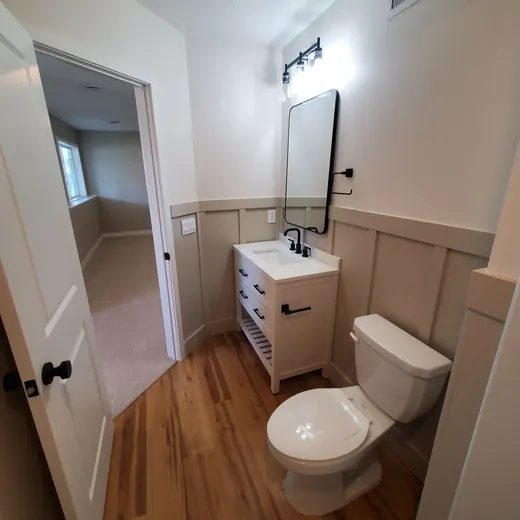 Small bathroom with toilet, sink vanity, mirror, and wood-look floor, viewed from the doorway