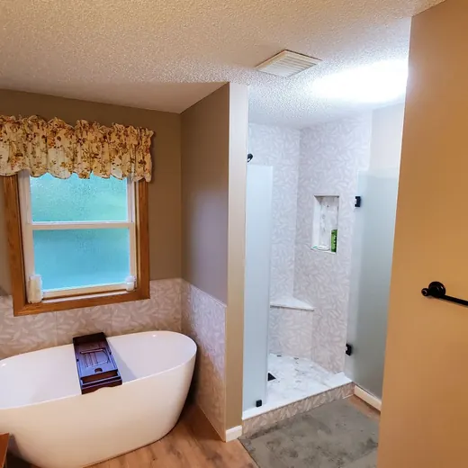 Small bathroom with a white freestanding tub, window, and adjoining glass shower.