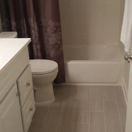 Small bathroom with white vanity, toilet, tub, and beige tile floor.