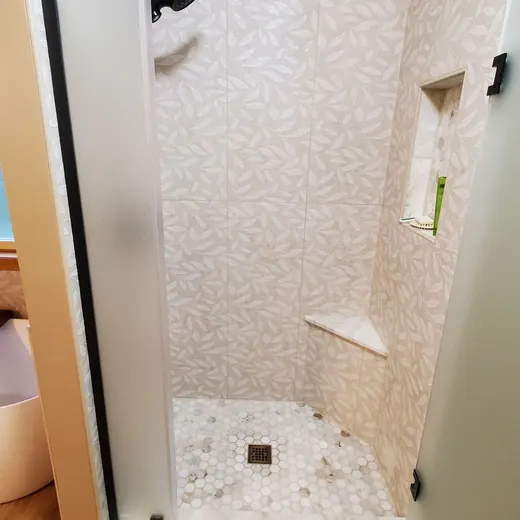 Small tiled shower stall with white walls, black fixtures, and a built-in corner shelf.