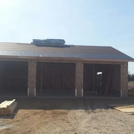 Small unfinished brick house with open window and door frames on a dirt lot under a bright sky.