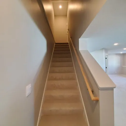 Steep carpeted staircase in a narrow hallway with beige walls and white railing.