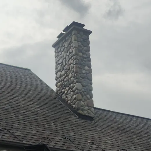 Stone chimney on a shingled roof against a cloudy sky.