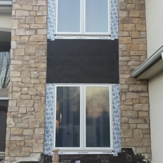 Stone house exterior with black siding, two windows, and a small fountain in front garden