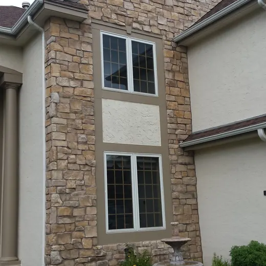 Stone townhouse facade with two windows, tan siding accents, and a landscaped front path