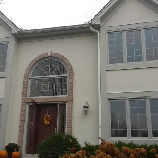 Two-story beige house with arched front window, double garage, and autumn decorations on the porch