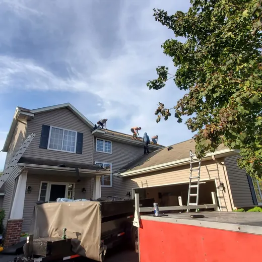Two-story house under renovation with scaffolding, tarp, and a red dumpster in the foreground