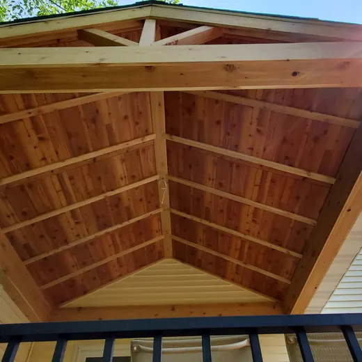 Underside of a wooden gable roof over a balcony, with sunlight at the peak