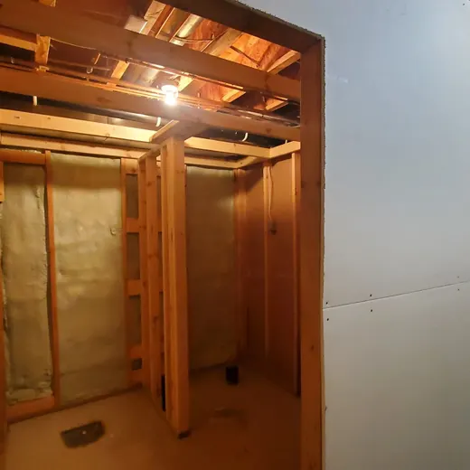 Unfinished home interior with exposed wooden framing and an open doorway to a hallway