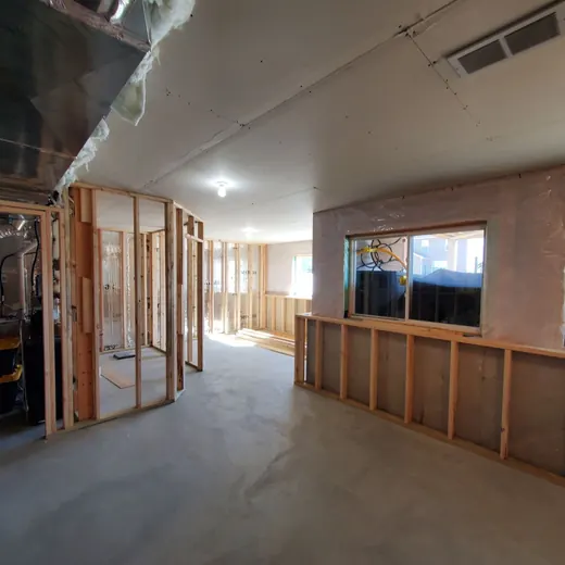 Unfinished interior of a building with exposed framing, concrete floor, and large windows letting in daylight