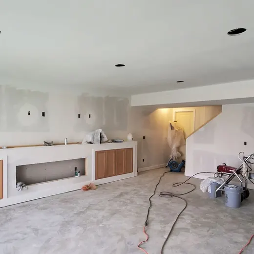 Unfinished kitchen with white cabinets, bare floor, and construction materials during renovation