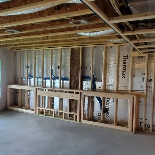 Unfinished room under construction with exposed wood framing, insulation, and windows letting in daylight