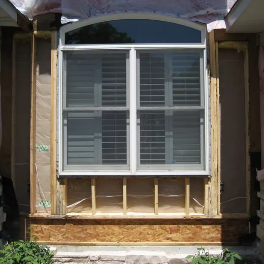 Window framed by unfinished wooden siding under a stone archway on a house exterior