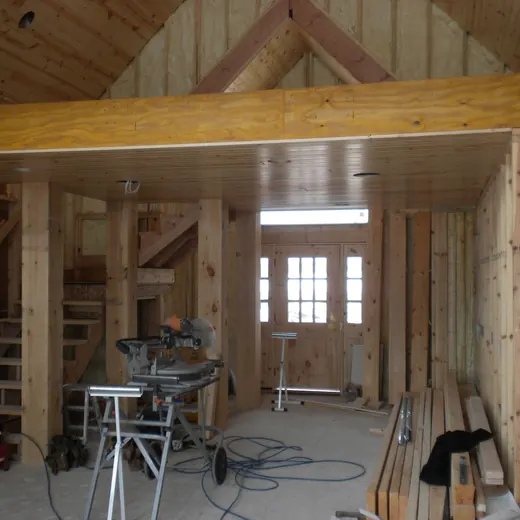 Wood-framed interior under construction with stairs, tools, and exposed beams