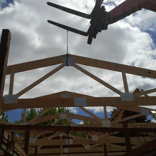 Wooden frame under construction against a cloudy sky, with a plane overhead.