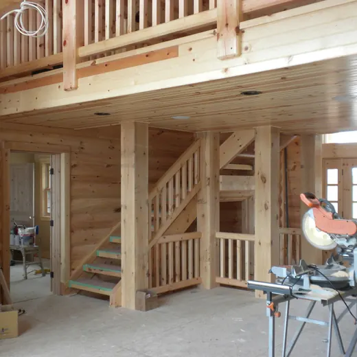 Wooden home interior under construction with stairs, loft, and a miter saw in the foreground