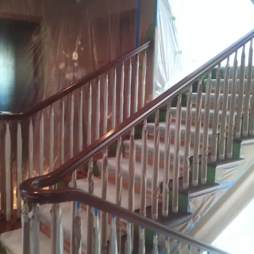 Wooden staircase with dark banister and white balusters in a sunlit interior.