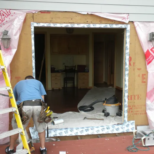 Worker installing trim around a large doorway opening in a partially renovated building