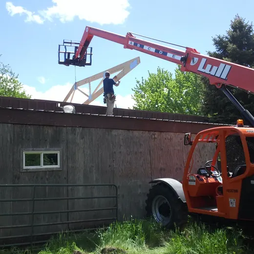 Worker on a red lift repairing a rooftop on a building beside a fenced yard.