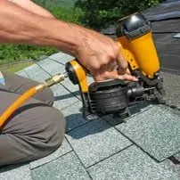 Worker using a yellow roofing nail gun to secure shingles on a roof
