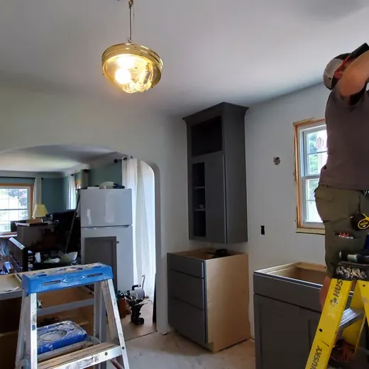 Worker on yellow ladder painting a kitchen ceiling in a partially renovated room.