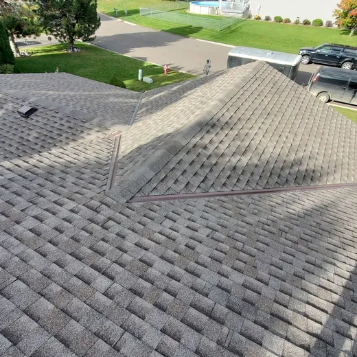 Workers repairing a gray shingle roof, with tools and materials on the rooftop and houses below.