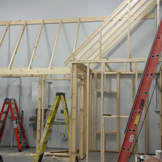 Workshop with unfinished wooden wall framing, ladders, and tools under construction.