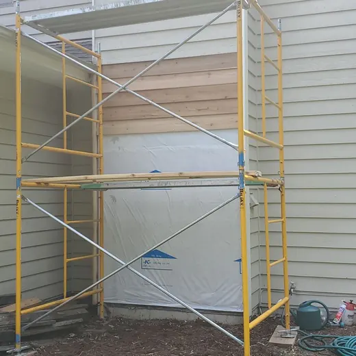 Yellow scaffolding beside a house exterior with a covered doorway under renovation