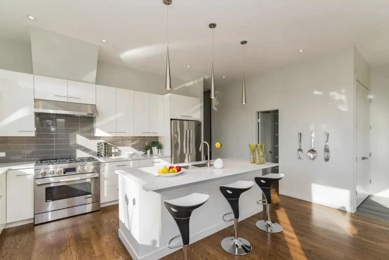 Bright modern kitchen with white island, stools, stainless appliances, and wood floors