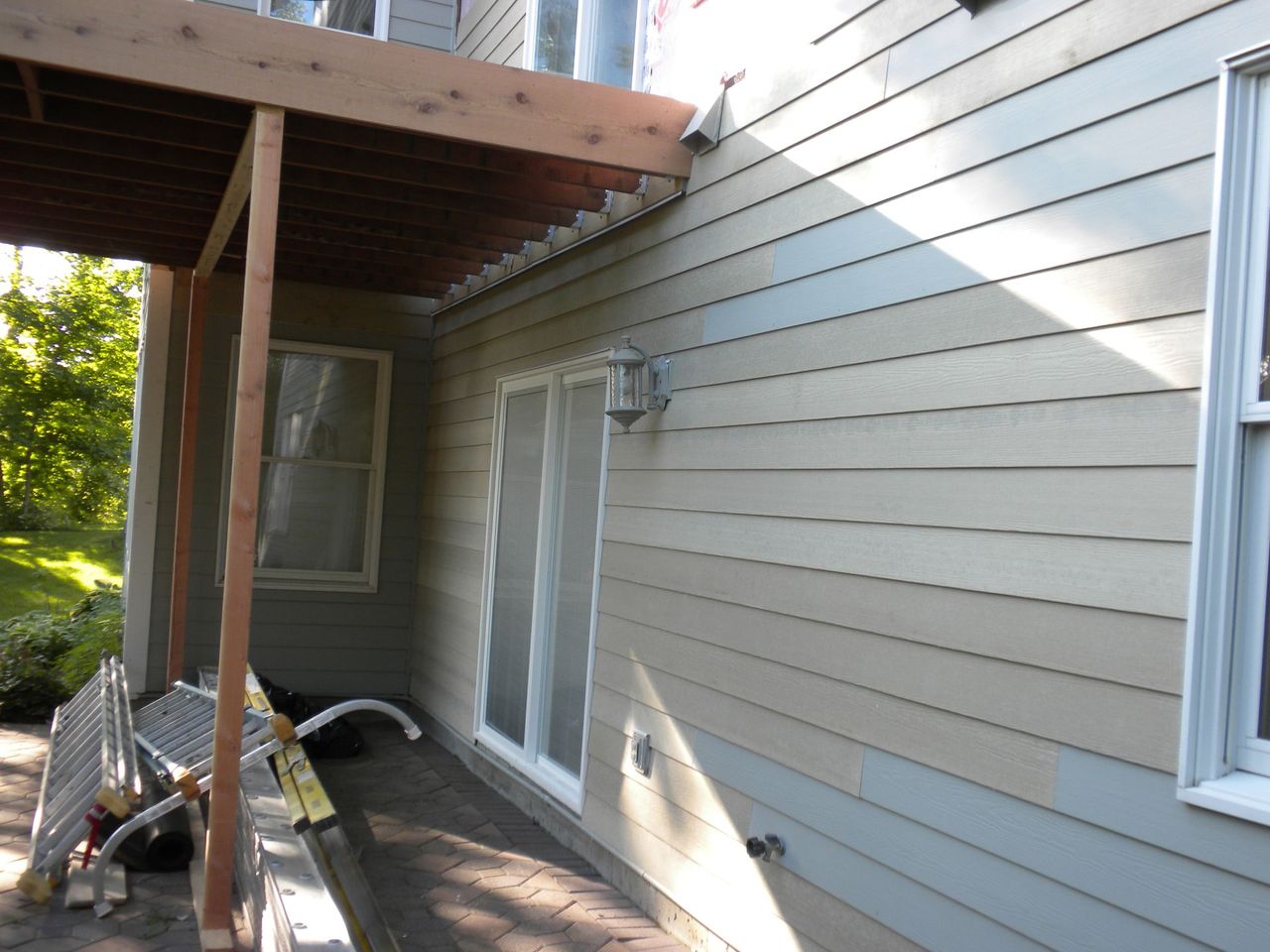 Back patio with beige siding, sliding glass door, and wooden deck roof in a shaded yard