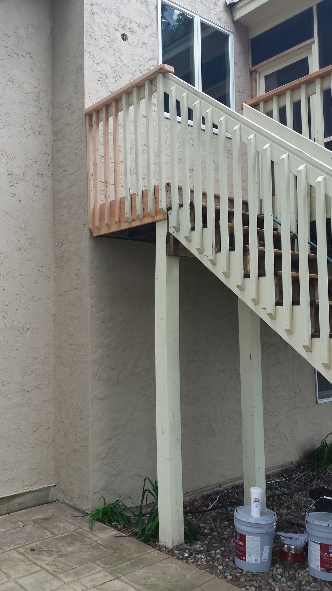 Exterior staircase with white railings beside a beige stucco building and a window, with buckets below.
