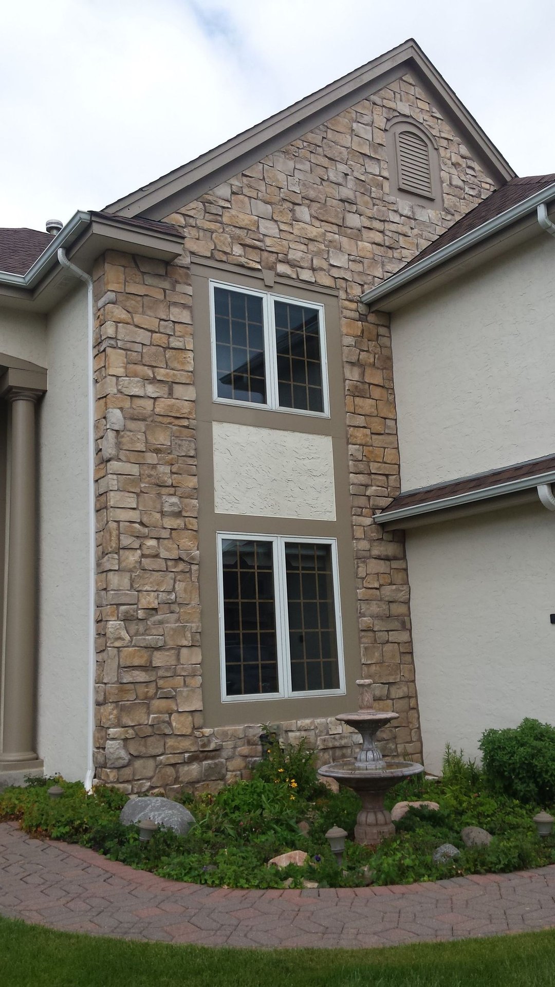 Stone townhouse facade with two upper windows, beige siding, and a landscaped front path